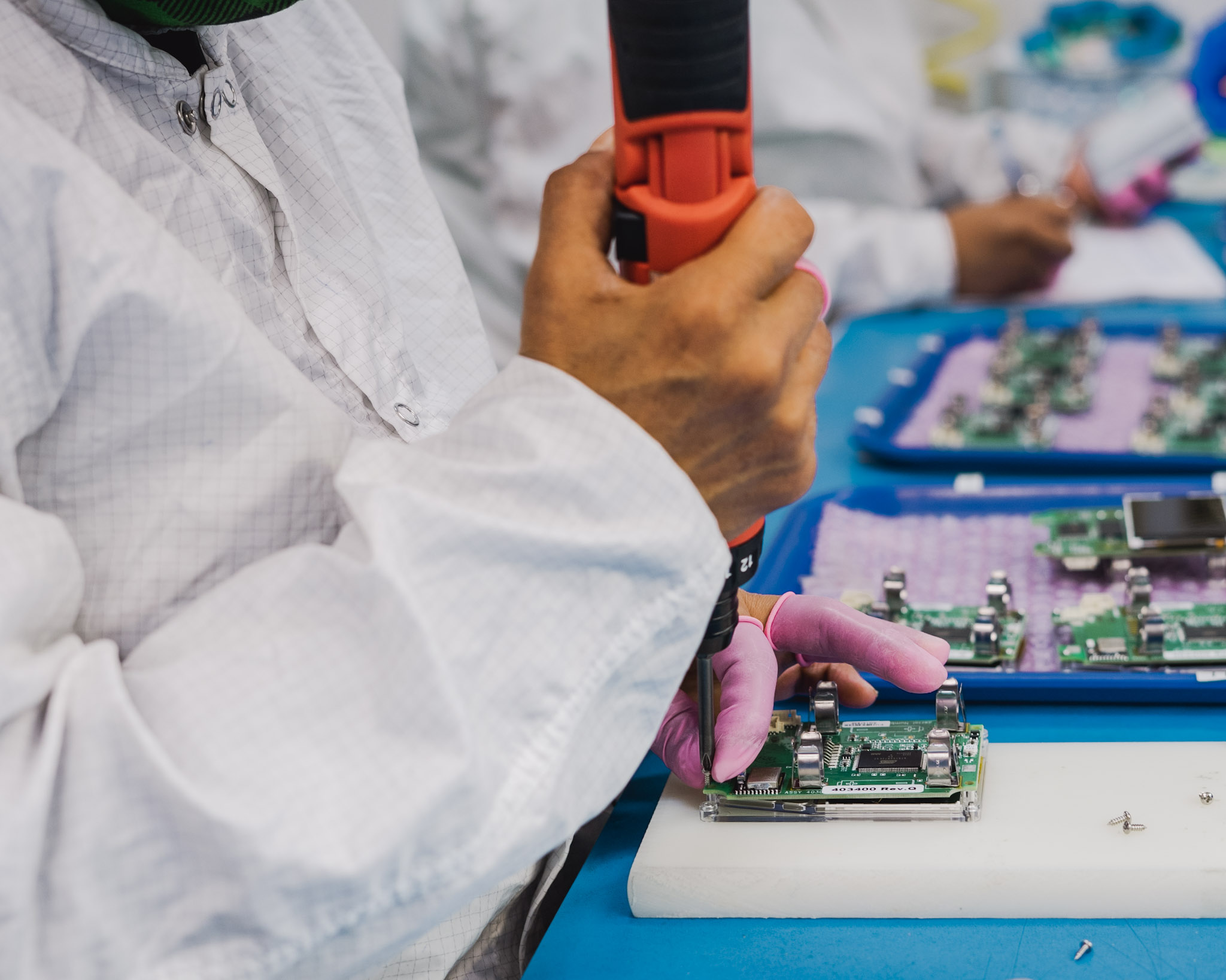 Technician assembling electronic components in a cleanroom environment with precise tools.