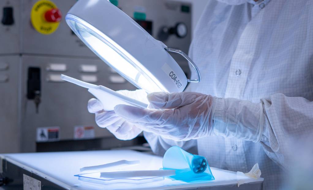 Technician inspecting medical device components with a magnifying lamp in a quality control lab.