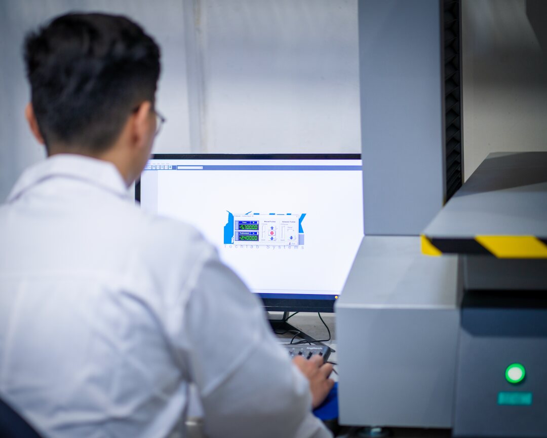 Technician reviewing accelerated aging test data on a computer in a controlled laboratory environment.