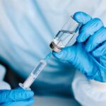 Gloved technician drawing liquid from sterile vial into syringe in cleanroom environment