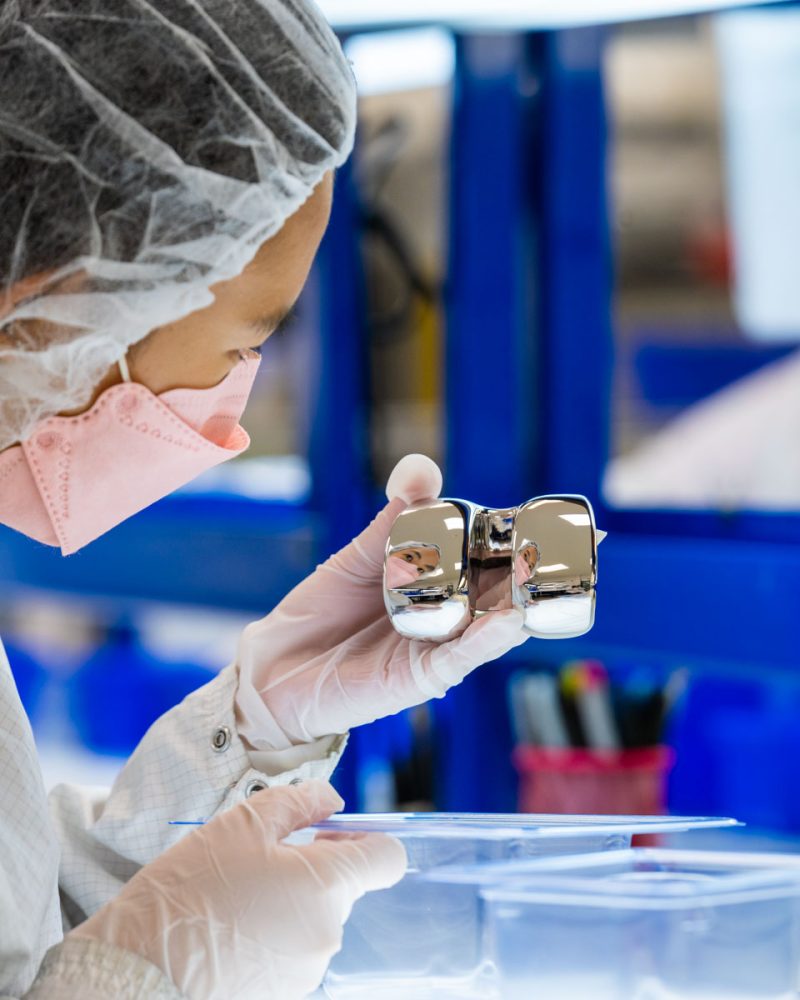 Sara Adachi in the Life Science Outsourcing cleanroom holding an orthopedic implant Sara Adachi in the Life Science Outsourcing cleanroom holding an orthopedic implant
