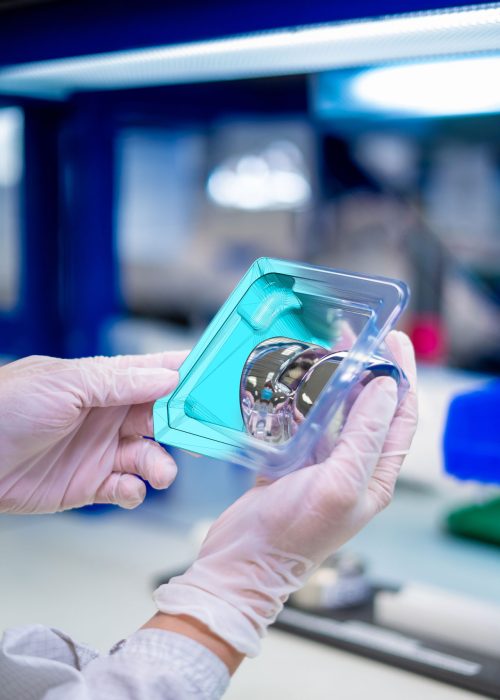 Gloved hands holding a packaged orthopedic implant in a cleanroom environment