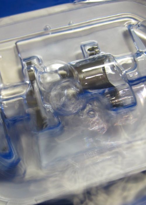 Hands submerging a custom rigid medical device tray in water during ASTM F2096 bubble emission testing, with visible air bubbles indicating a leak.