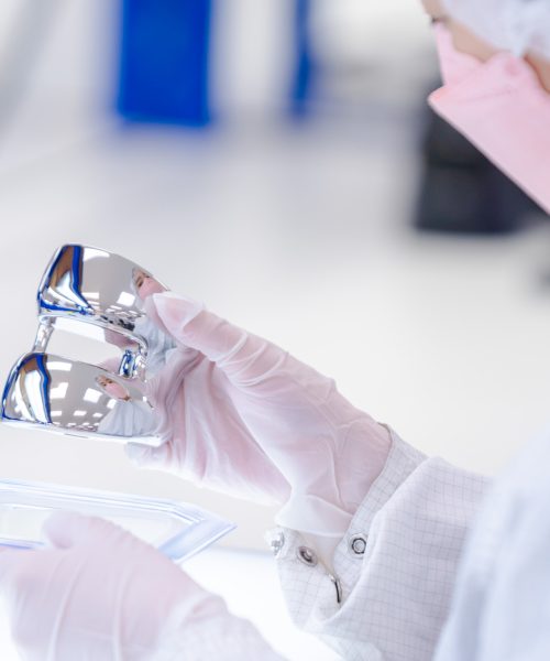 Lab Technician Inspecting Medical Device Component | Life Science Outsourcing Close-up of a lab technician in sterile cleanroom attire inspecting a polished medical device component at Life Science Outsourcing.