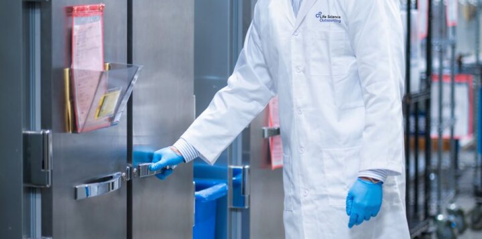 Technician in a white lab coat handling an aging test chamber in a laboratory for medical device packaging validation.