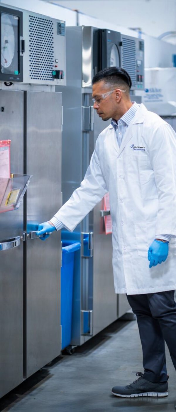 Technician in a white lab coat handling an aging test chamber in a laboratory for medical device packaging validation.