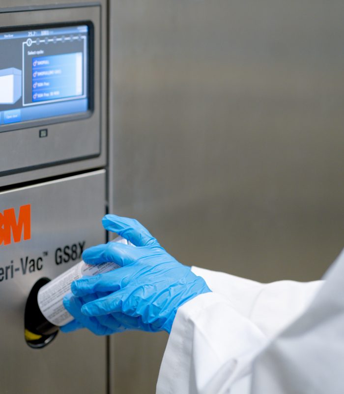 Close-up of a gloved hand placing a EtO sterilization canister into a 3M Steri-Vac GS8X system.