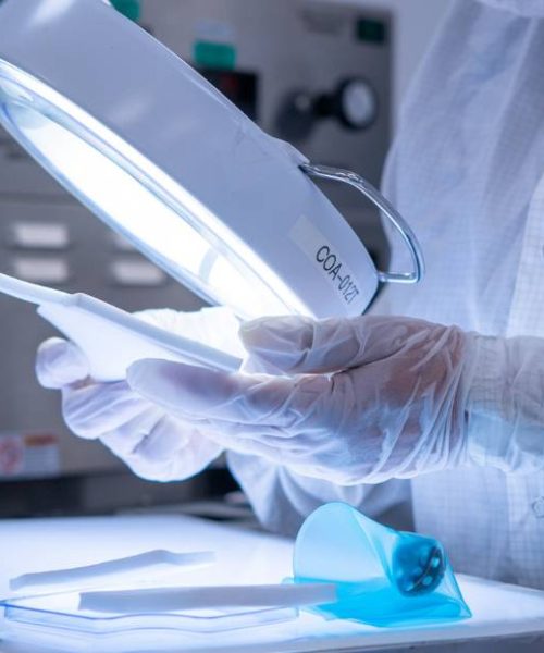 Technician inspecting medical device components with a magnifying lamp in a quality control lab.