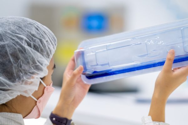 Technician wearing protective gear closely examining medical device packaging for leaks during a dye test in a laboratory setting.