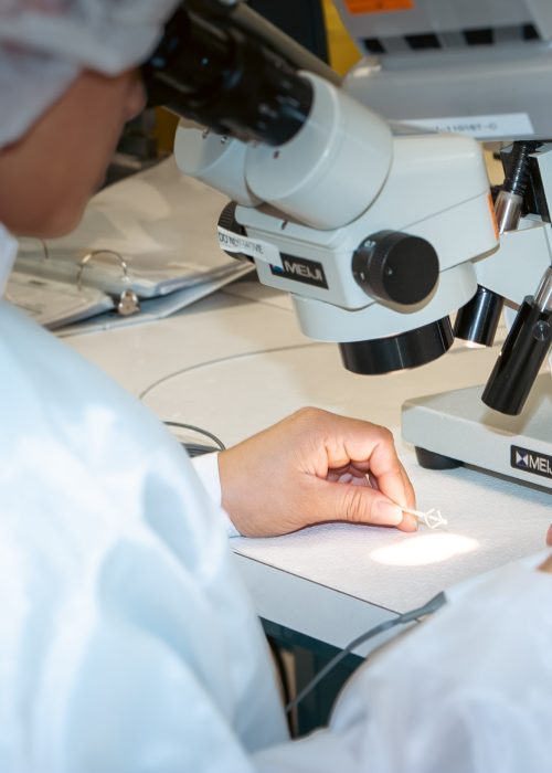 Technician assembling a micro-scale medical device component under a microscope in a cleanroom