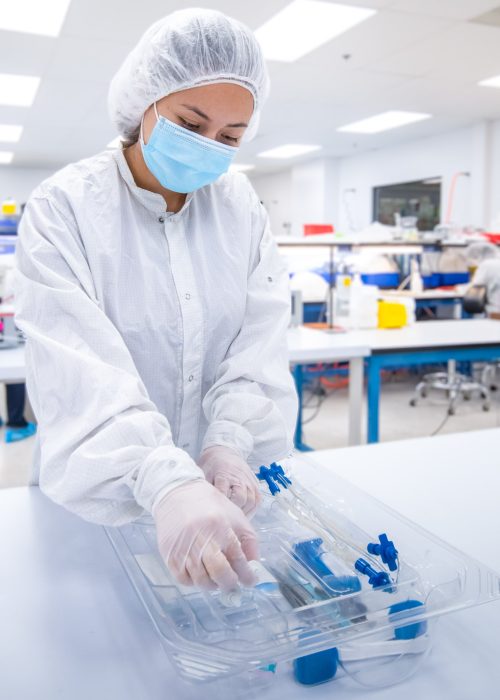 Technician Assembling Fluid Management Device in Cleanroom – LSO Technician in cleanroom assembling a sterile fluid management device kit, wearing full PPE including gown, mask, and gloves.