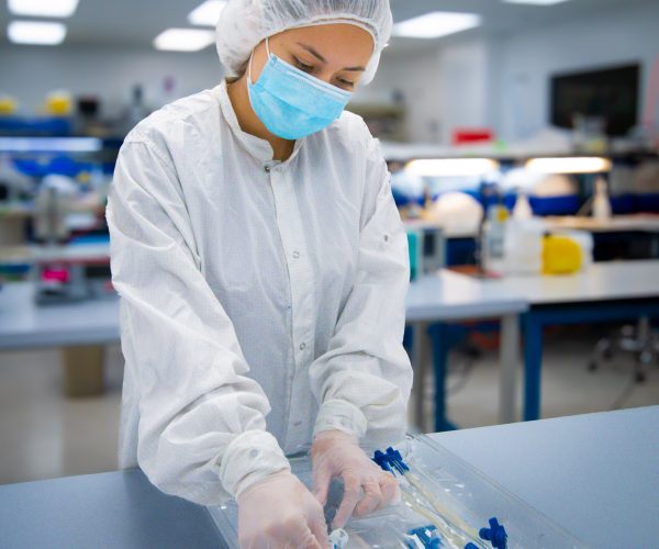 Technician Assembling Fluid Management Device in Cleanroom – LSO Technician in cleanroom assembling a sterile fluid management device kit, wearing full PPE including gown, mask, and gloves.