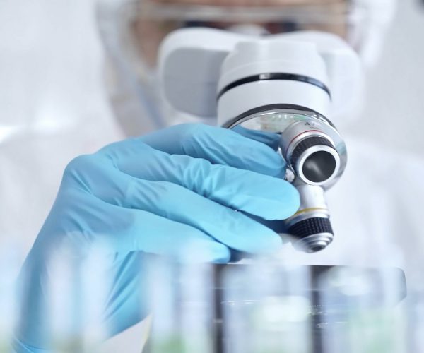Scientist examining microbial samples under a microscope in a sterile lab environment for medical device testing.