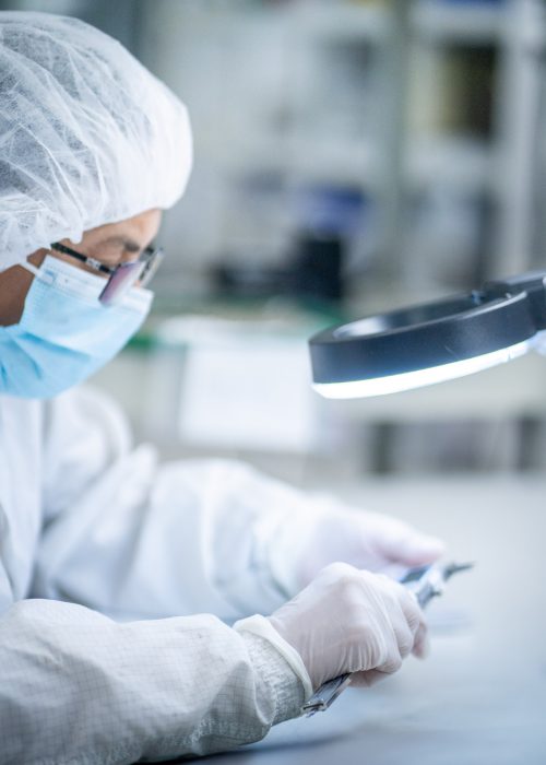 Cleanroom Inspection During Medical Device Assembly Technician inspecting a medical device under magnification in a cleanroom environment at LSO