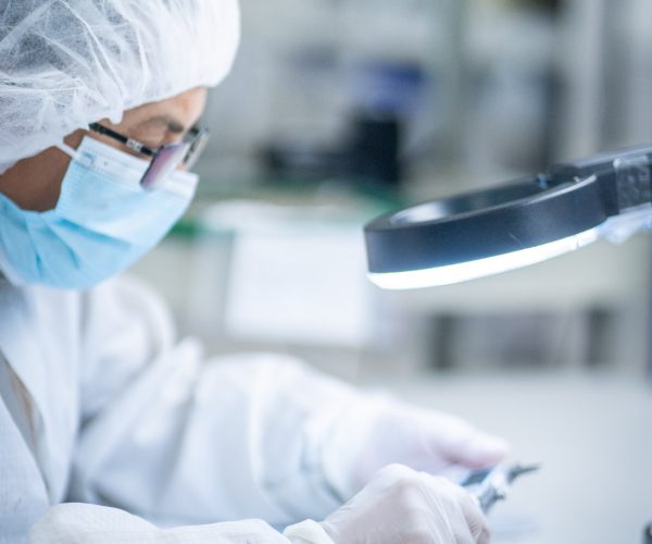 Cleanroom Inspection During Medical Device Assembly Technician inspecting a medical device under magnification in a cleanroom environment at LSO