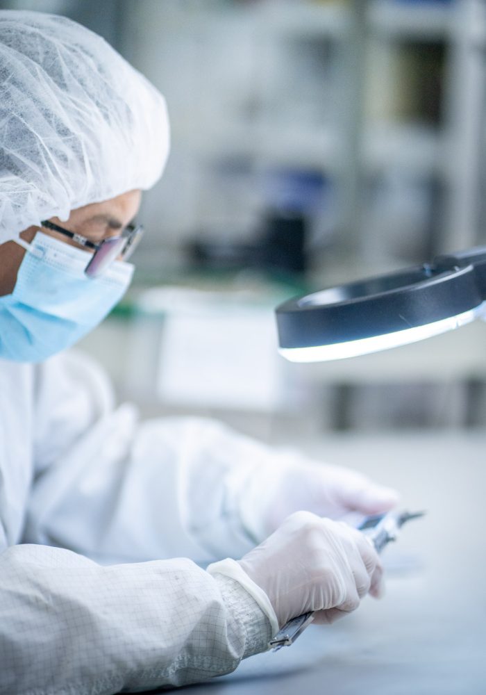 Technician inspecting a medical device under magnification in a cleanroom environment at LSO
