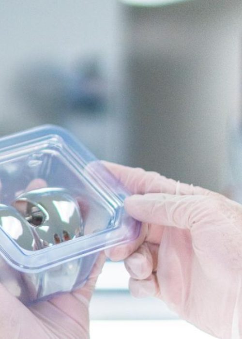 Gloved hands holding a sterile medical device in clear packaging.