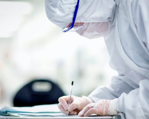 LSO Medical Device Assembly Quality Supervisor meticulously reviewing documentation in a pristine cleanroom to ensure optimal production standards.
