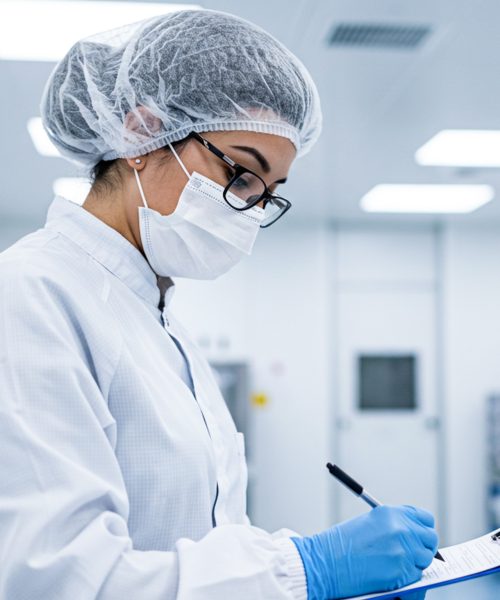 Quality Control Inspection in a Cleanroom Environment A laboratory technician in cleanroom attire conducts a quality control inspection with a clipboard and pen in a sterile facility.