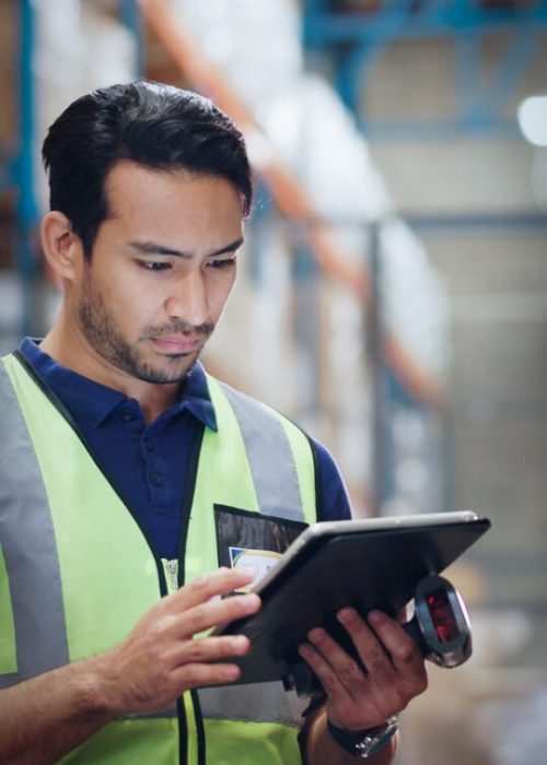 Warehouse worker in a safety vest using a tablet and barcode scanner for inventory tracking