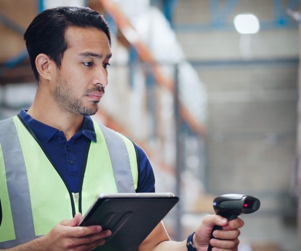Warehouse Worker Using Digital Inventory Management Warehouse worker in a safety vest using a tablet and barcode scanner for inventory tracking