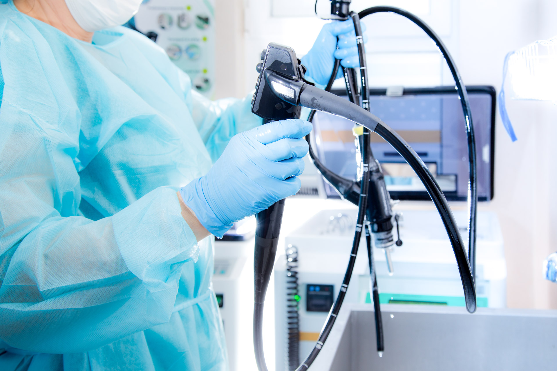 Technician in PPE handling a flexible endoscope in a sterile environment, representing gastroenterology device care and processing.