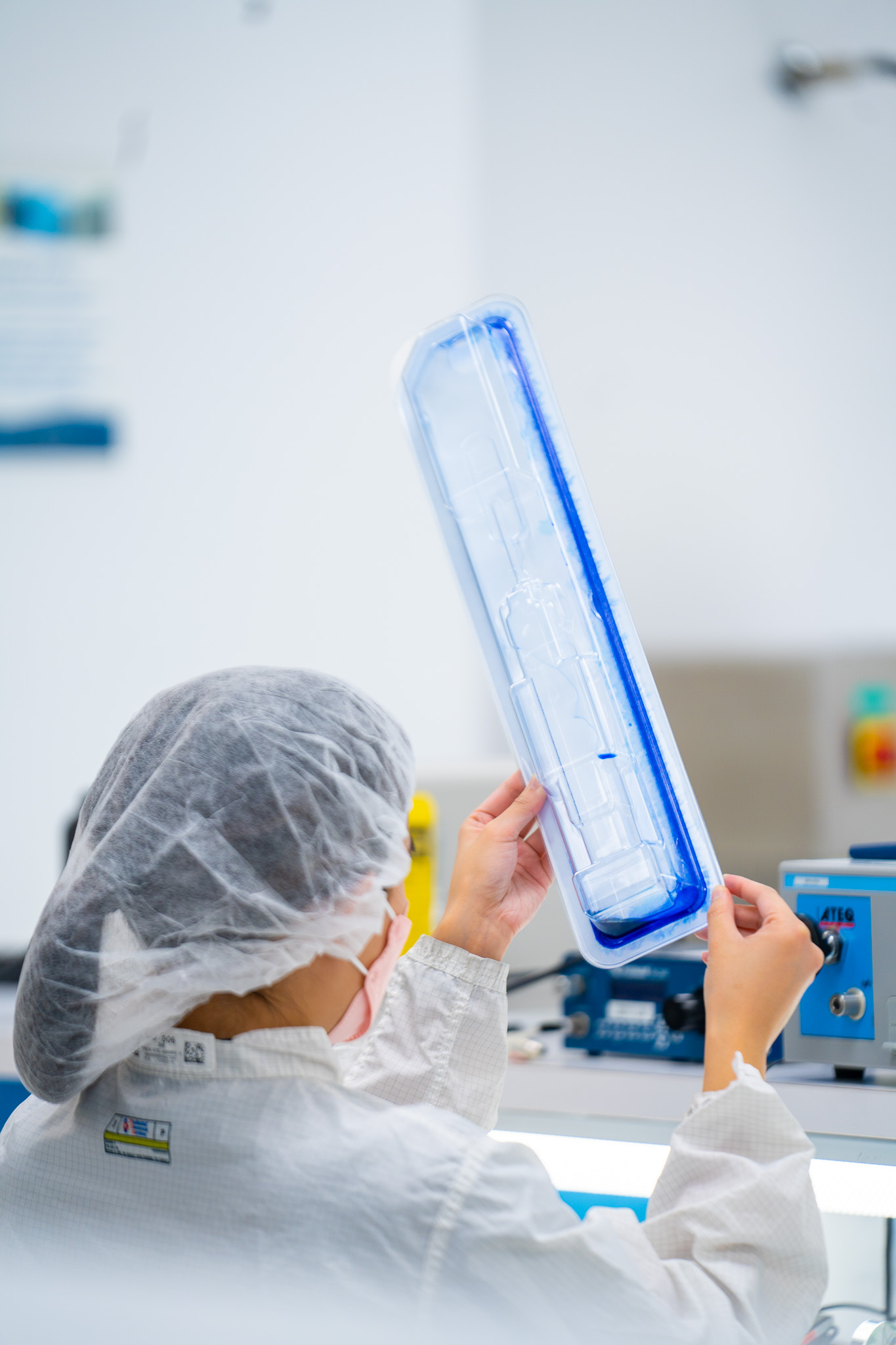 A laboratory technician in a cleanroom inspecting a medical device tray for seal integrity using blue dye penetration testing.