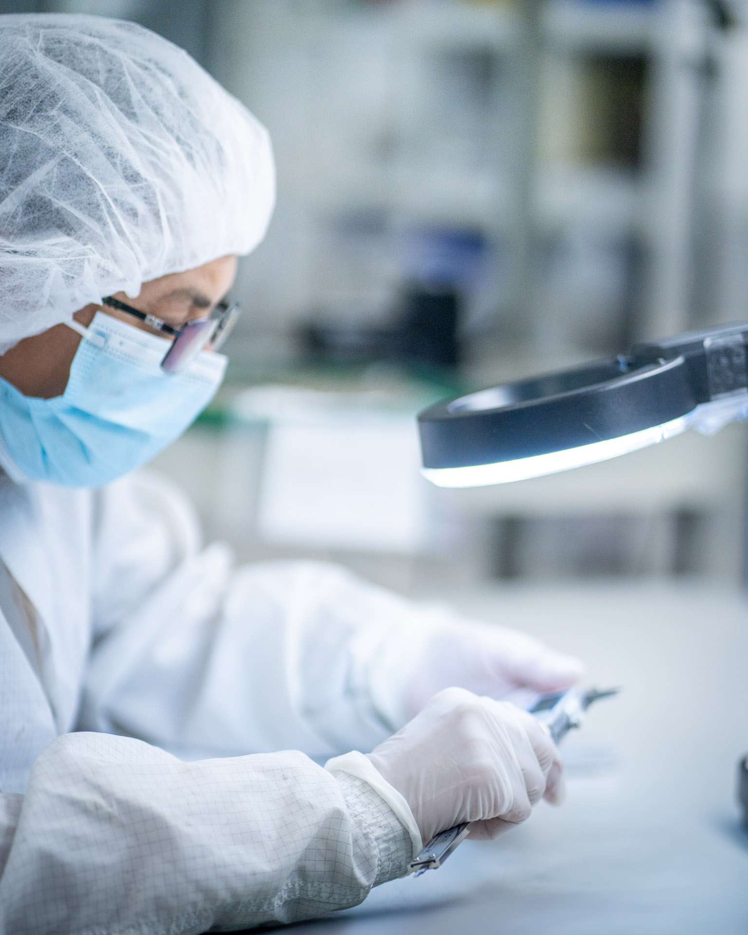 Technician inspecting a medical device under magnification in a cleanroom environment at LSO