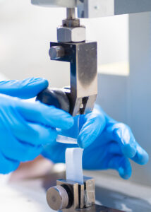 A close-up of a laboratory technician performing a peel strength test on medical packaging using a tensile testing machine, following ASTM F88 standards.
