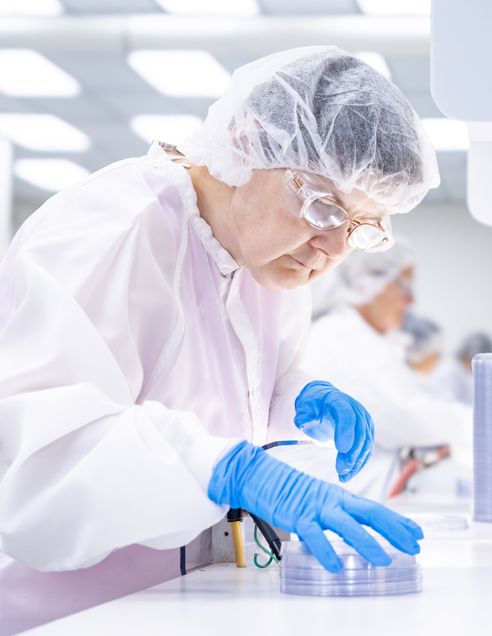 Cleanroom technician wearing protective gear carefully handling stacked thermoformed trays.